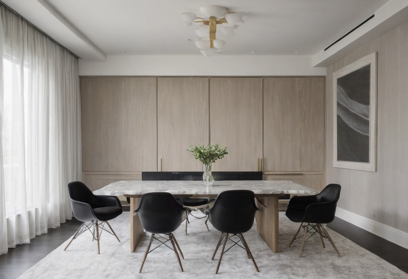 A meeting room with pale oak panelling, a white marble table on a chunky oak base, four black moulded chairs, a vase of white flowers and a sculptural ceiling light.